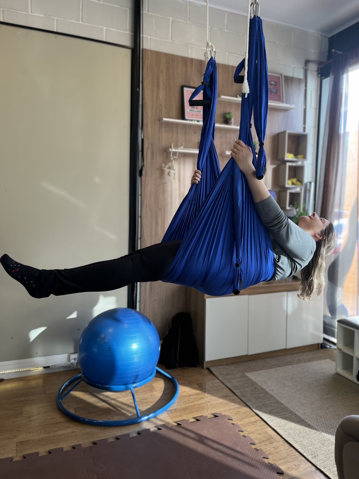 Aluna apoiada na rede de Pilates aéreo, ao lado da bola suíça do estúdio